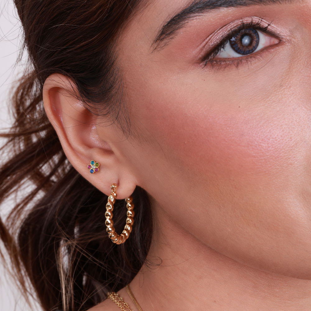 Close-up of a woman's ear wearing a gold hoop earring and a small multicolor flower stud earring.
