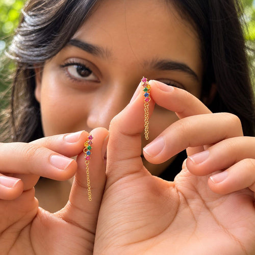 A close-up of a girl holding a pair of 18k gold plated sterling silver multicolour zicon chain stud earrings