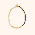 A gold paperclip chain bracelet with one half embellished with small black stones, displayed on a light cream background.