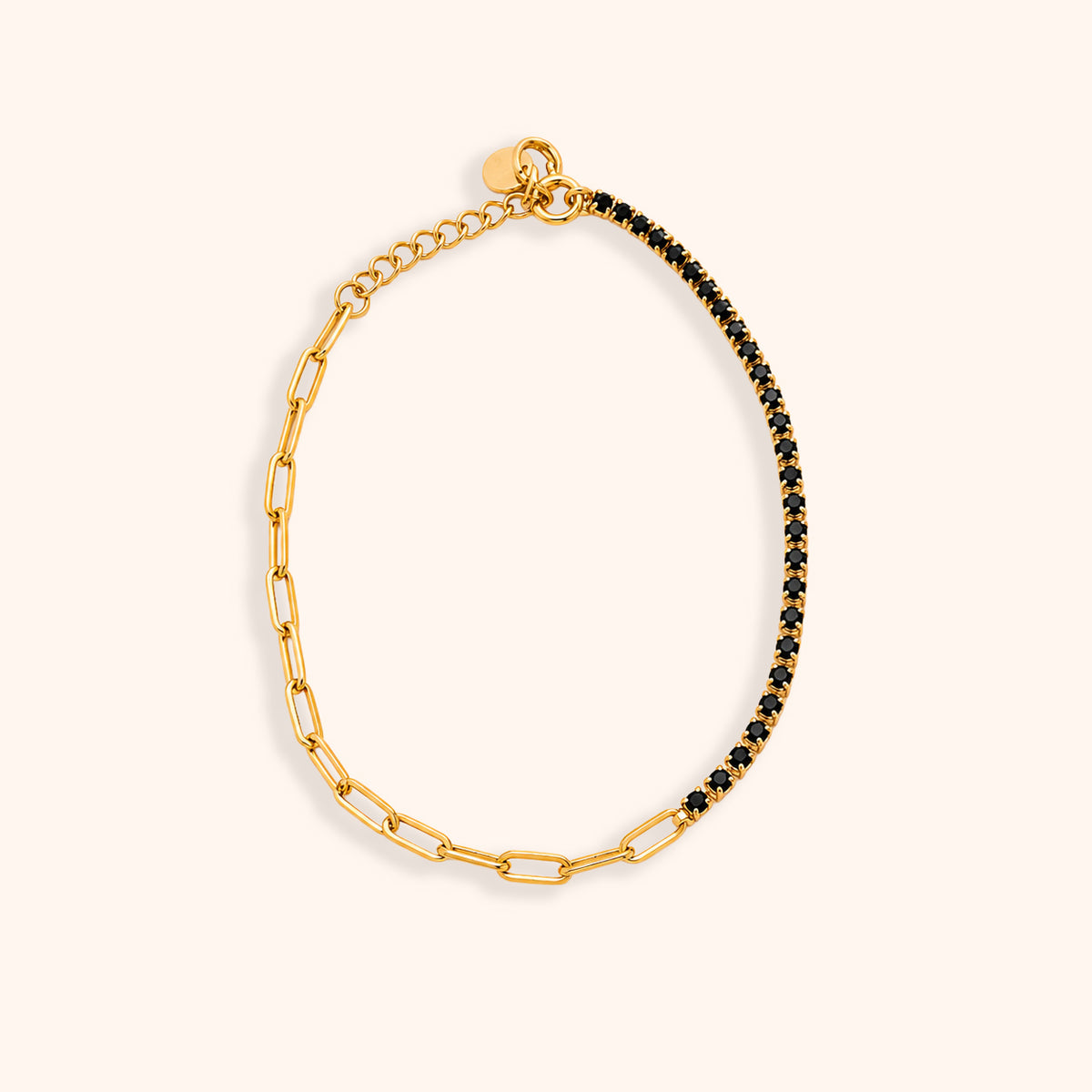 A gold paperclip chain bracelet with one half embellished with small black stones, displayed on a light cream background.