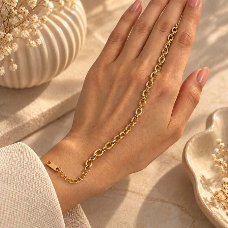 A delicate gold chain bracelet close up with elongated oval links and a small clasp, shown worn on a woman's wrist. 