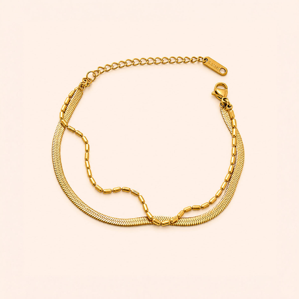 A gold-tone chain bracelet with a textured snake-link style chain, a beaded chain section, and an adjustable lobster clasp, displayed on a light cream background.