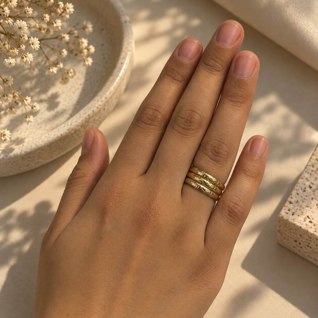 A close-up of a hand wearing 18K gold plated Twist Statement ring, styled with dried flowers and warm natural light on a beige surface.