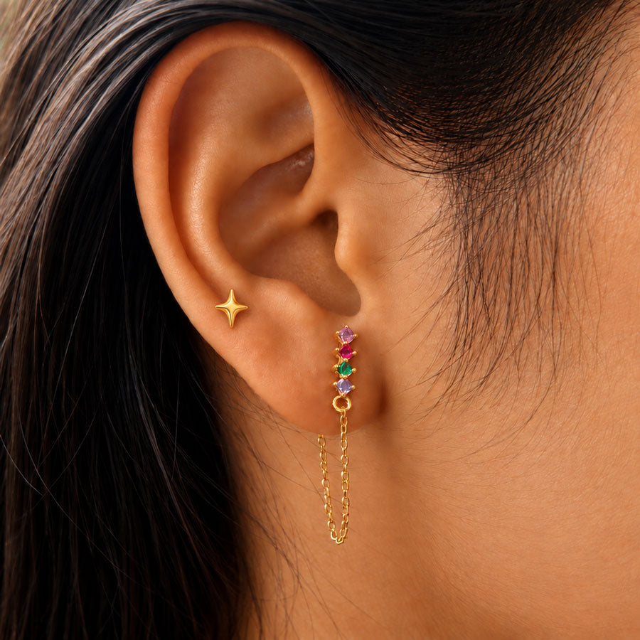 A close-up of a model wearing a golden nova ear stud with a dangling multicolor gemstones chain earrings.